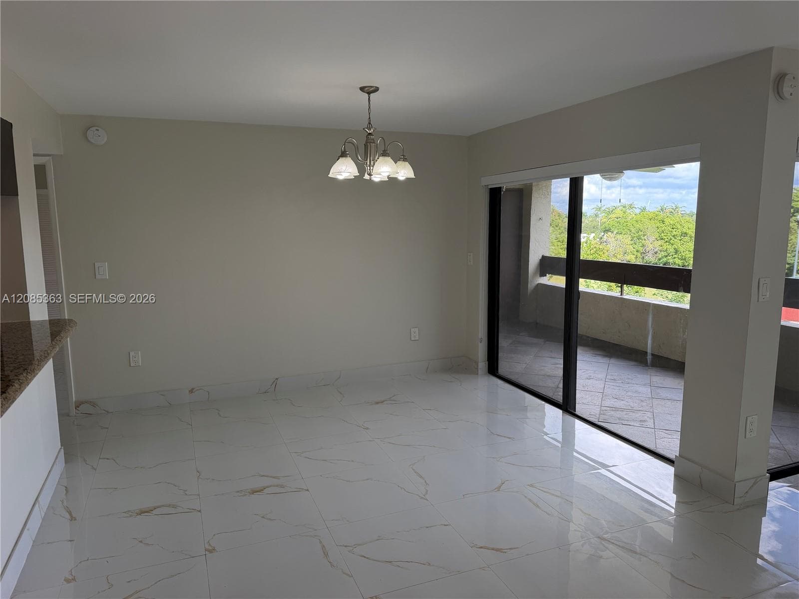 Large-format light-toned tile flooring with veining, multi-arm chandelier, and sliding glass doors leading to a covered balcony