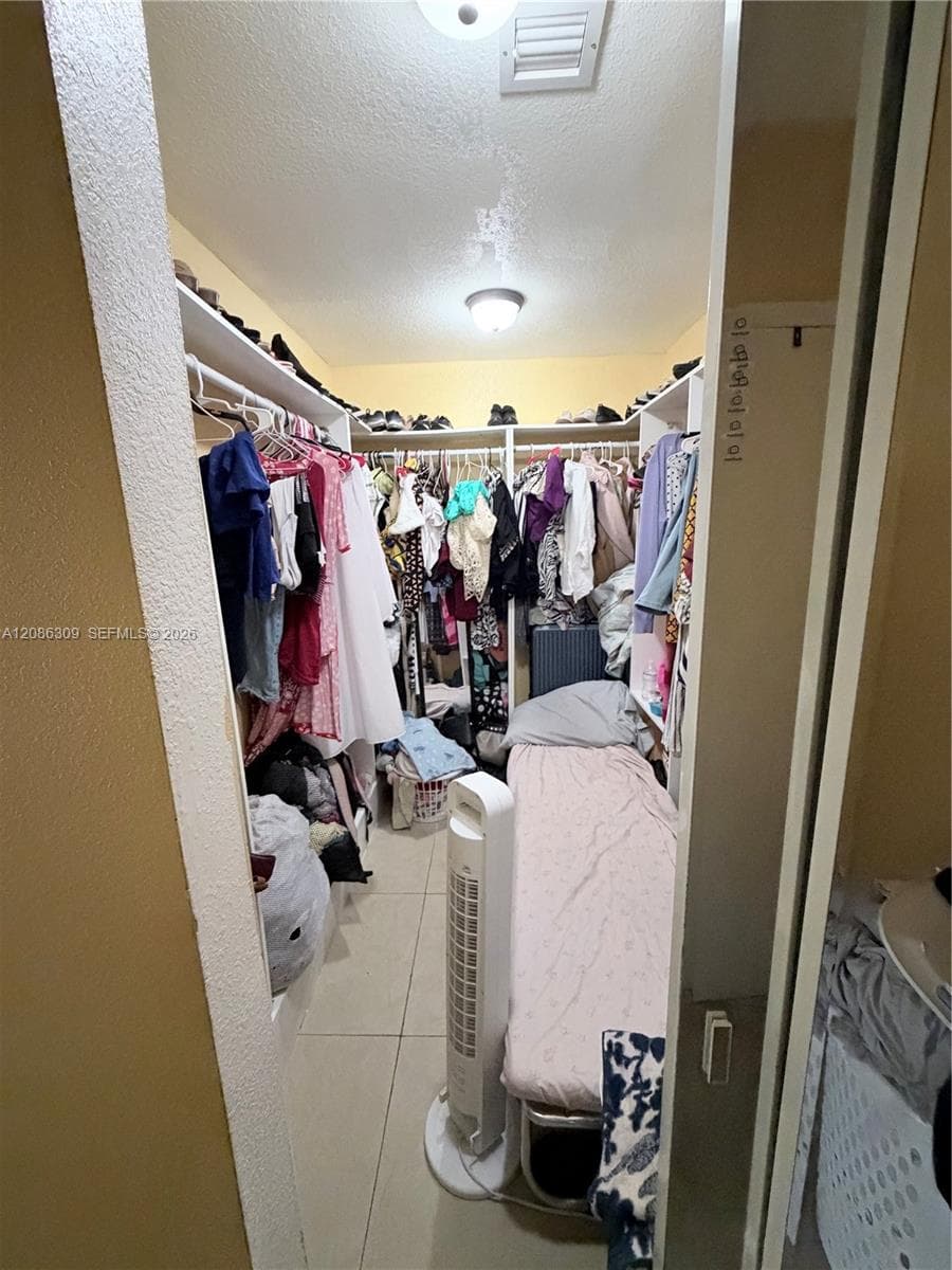 Walk-in closet featuring floor-to-ceiling built-in shelving, hanging rods, and ceramic tile flooring
