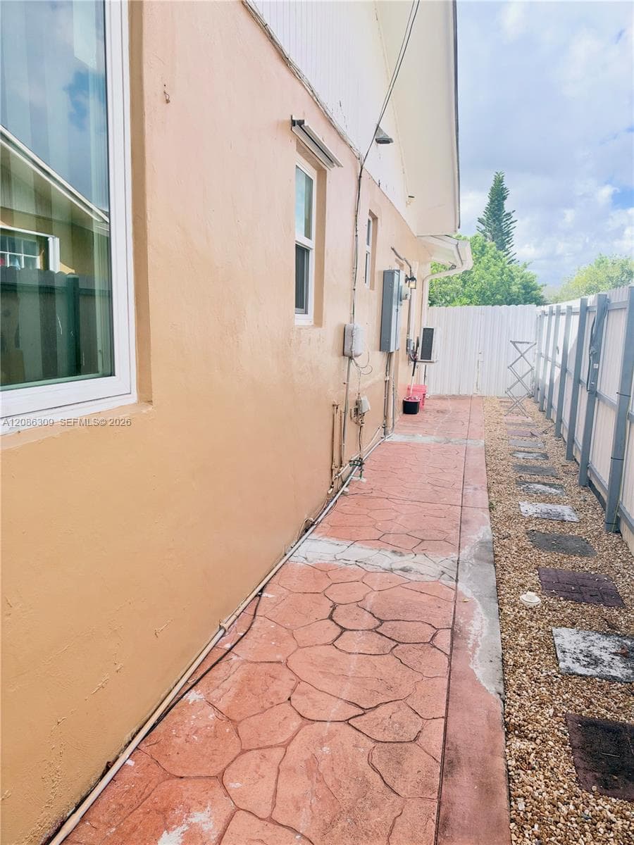 Exterior side yard featuring a stamped concrete walkway, white vinyl perimeter fencing, and stone-accented ground cover
