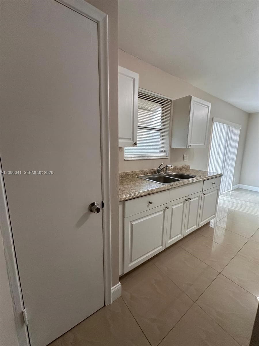 Kitchen featuring white cabinetry, stone-finish countertops, stainless steel dual-basin sink, and polished tile flooring