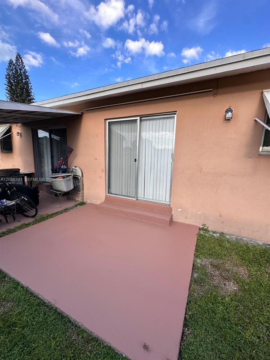 Rear exterior featuring a concrete patio, sliding glass door, metal awning, and exterior wall-mounted lighting