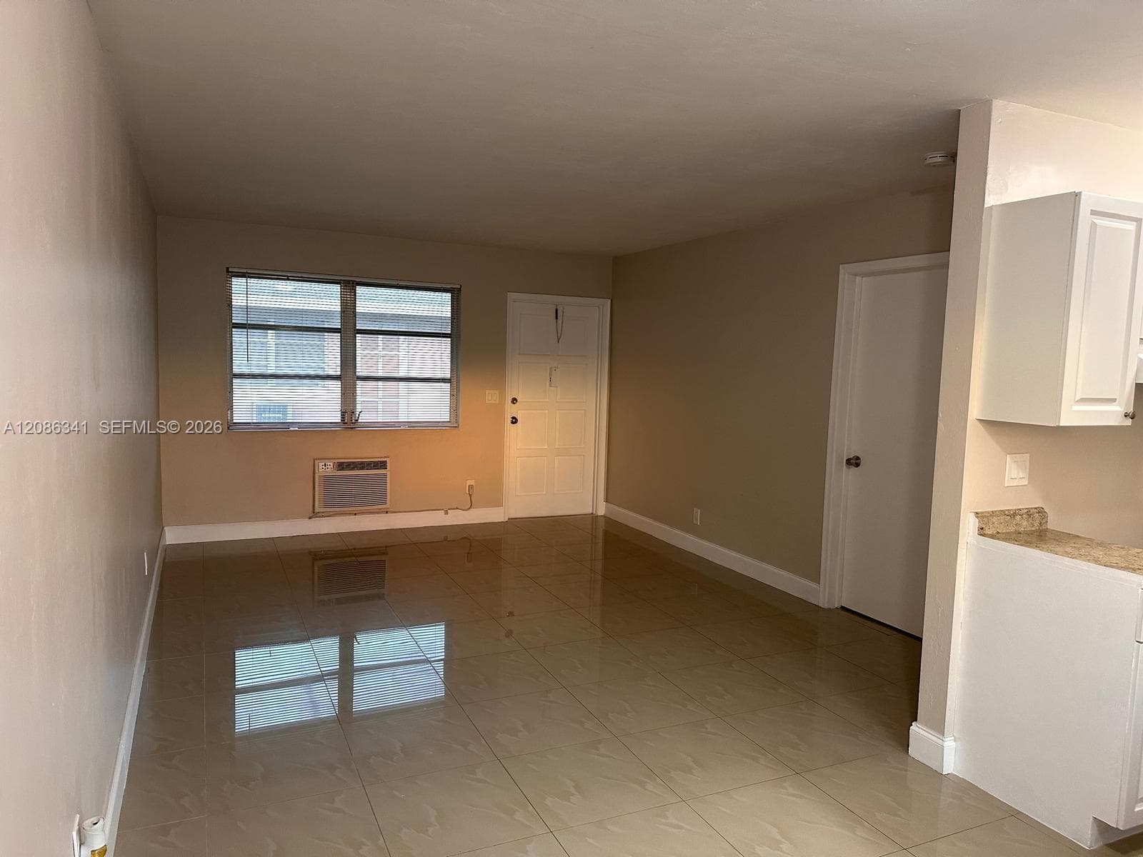 Neutral-toned interior space featuring large-format tile flooring, multi-pane window, wall-mounted air conditioning unit, and solid-core interior doors