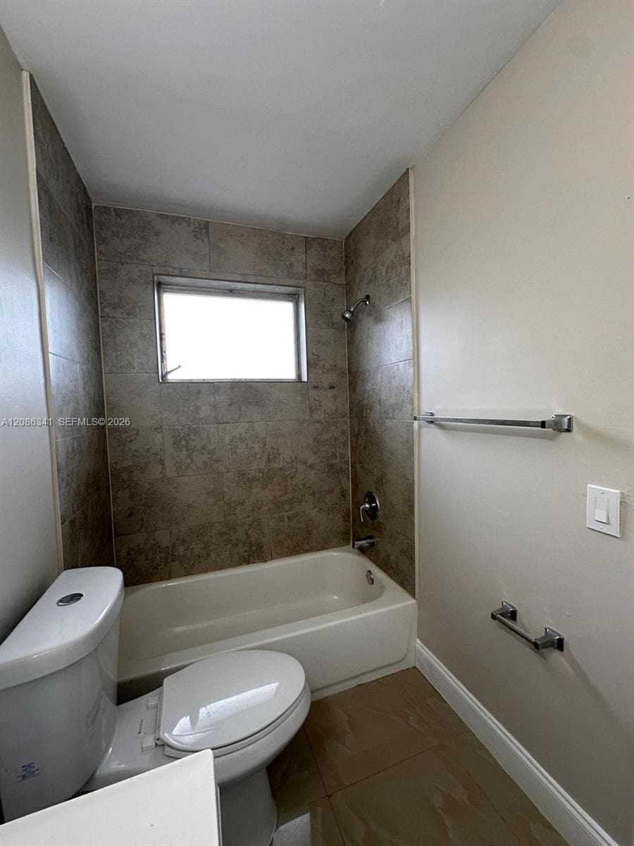 Bathroom featuring a full-size bathtub, tile surround, integrated shower fixture, and polished metal hardware