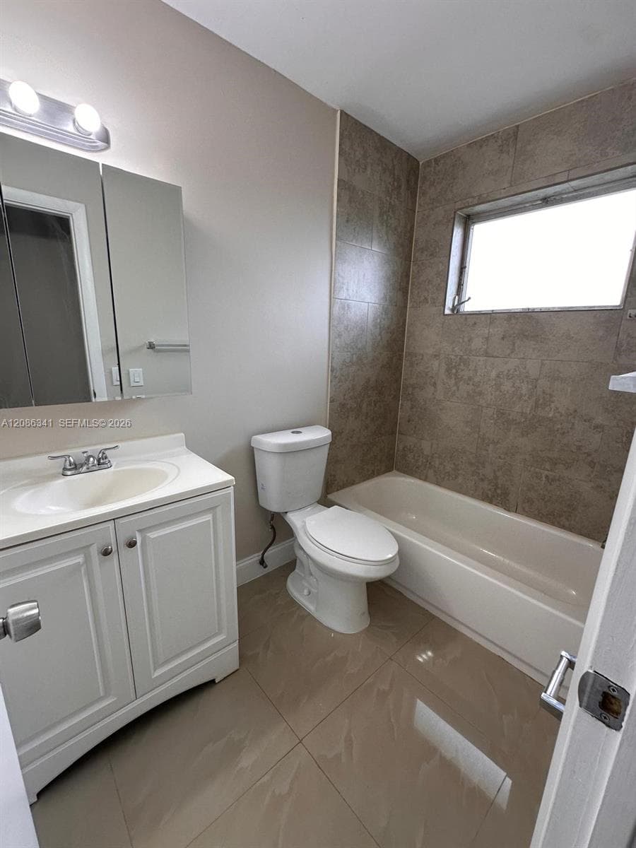 Bathroom featuring a white vanity cabinet, large-format tile flooring, a tub-shower combination with floor-to-ceiling surround tile, and an integrated mirrored medicine cabinet