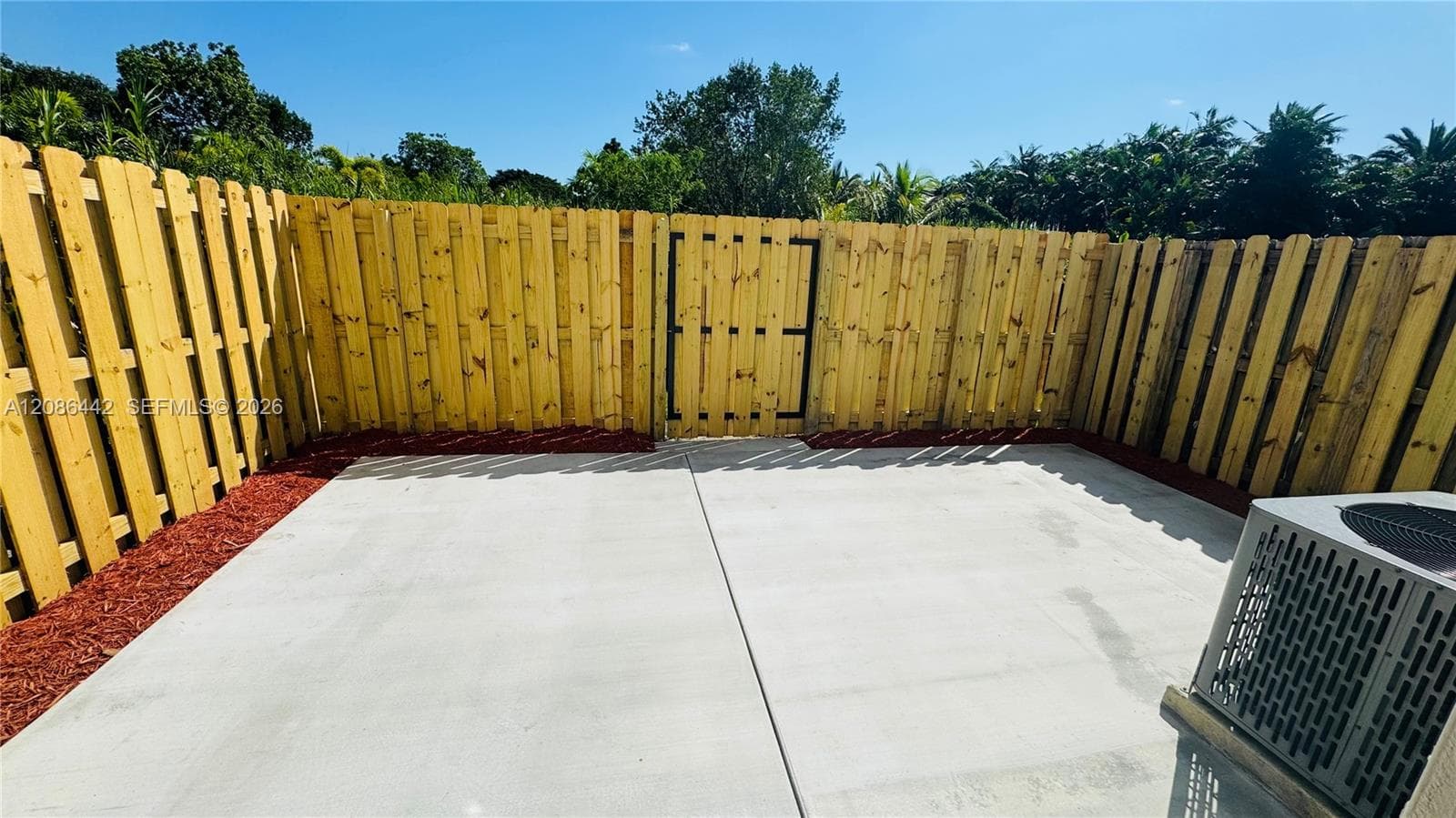 Concrete patio bordered by wood fencing, a locking wooden gate, and a foundation of mulch