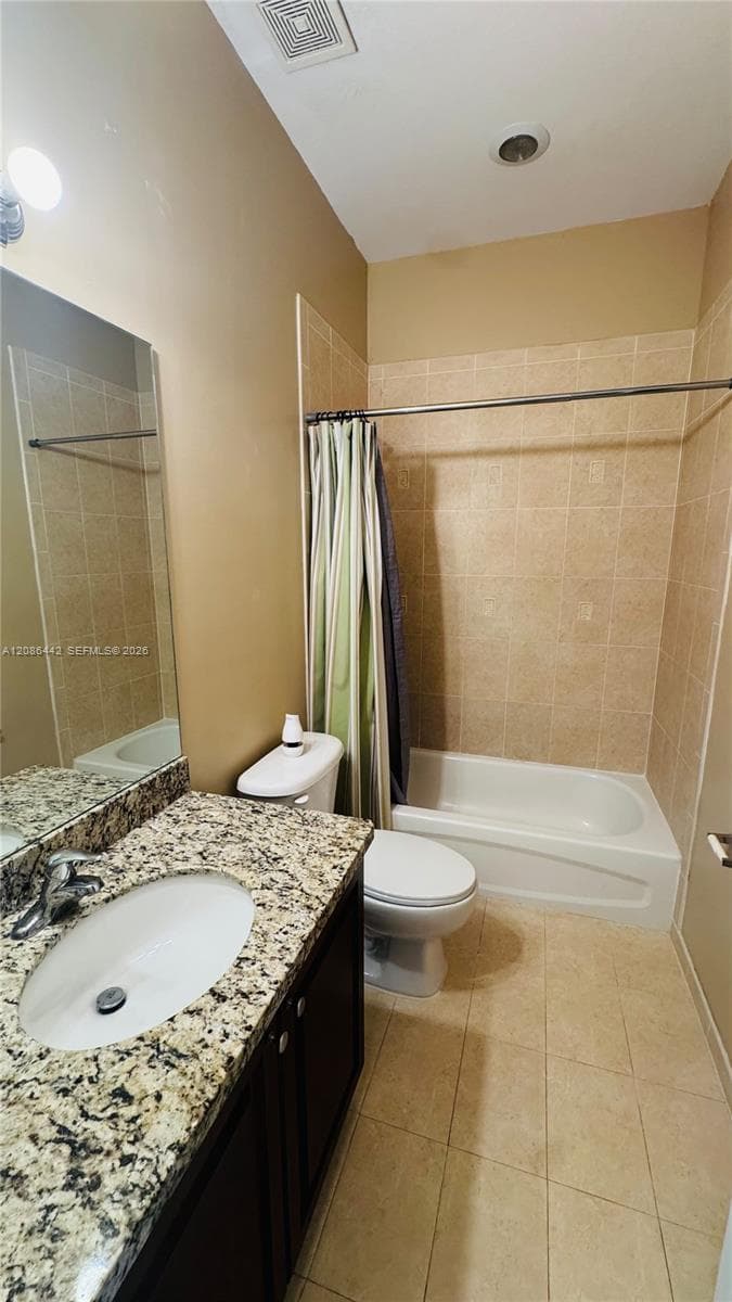 Bathroom featuring a vanity with a stone-patterned countertop, an integrated sink, dark cabinetry, and a tub-shower combination with tile surround and neutral tile flooring