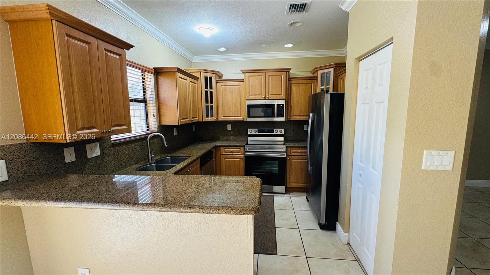 Kitchen featuring wood cabinetry, stone countertops, tile flooring, crown molding, and stainless steel appliances