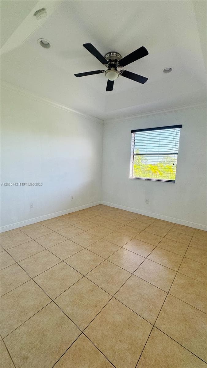 Tray ceiling featuring a central five-blade ceiling fan, recessed lighting, neutral tile flooring, and a single-pane window