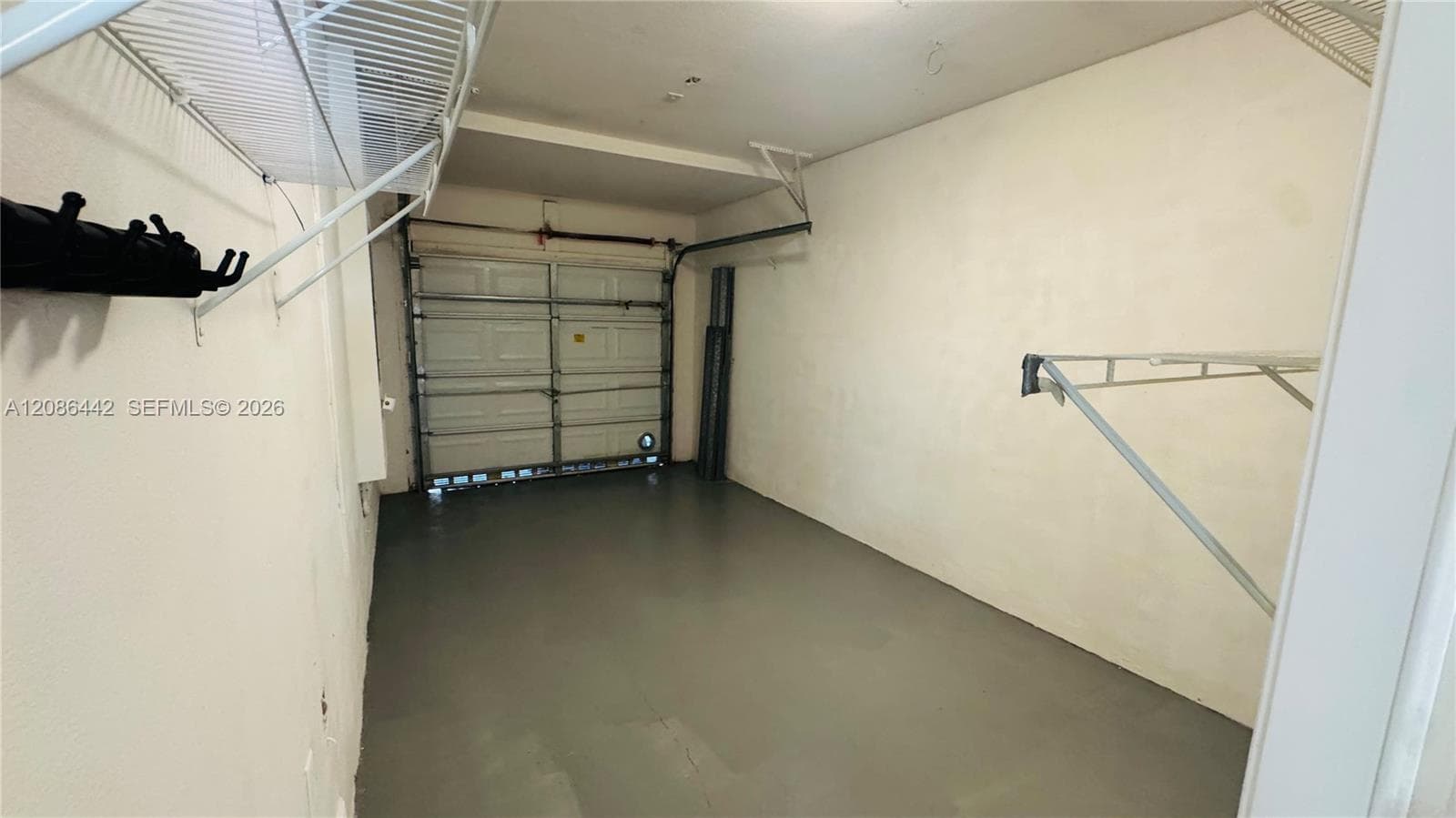 Enclosed garage featuring painted concrete flooring, a sectional roll-up door, and installed wire wall shelving