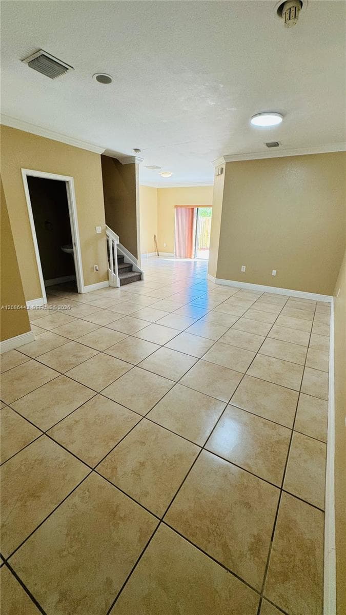 Neutral-toned ceramic tile flooring, recessed ceiling lighting, staircase with white wooden balustrade, and sliding glass door