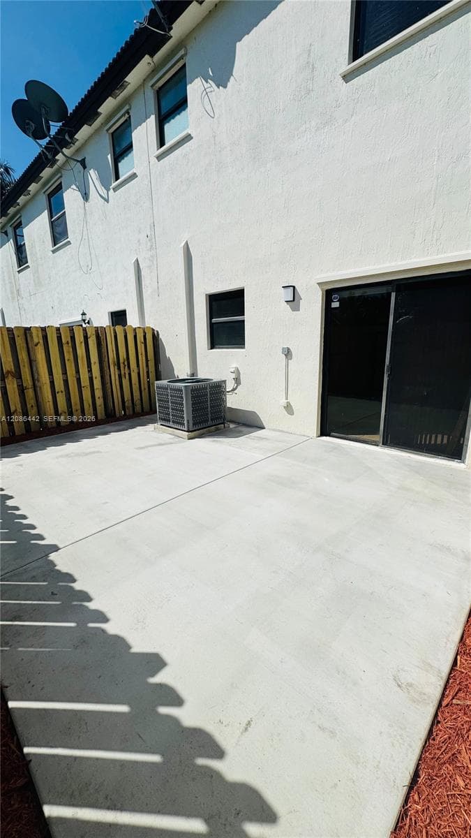 Concrete patio featuring a privacy fence, exterior sliding glass door, and stucco siding