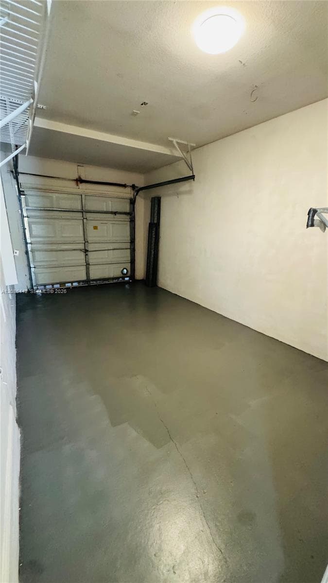 Enclosed garage featuring painted concrete flooring, a sectional overhead door, overhead lighting, and built-in upper shelving
