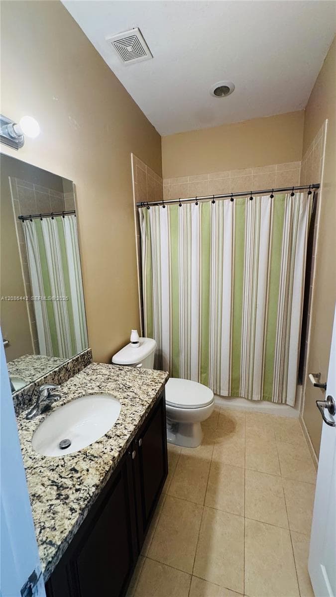 Bathroom featuring a stone-finish countertop, dark-finish cabinetry, an oval undermount sink, and tiled flooring