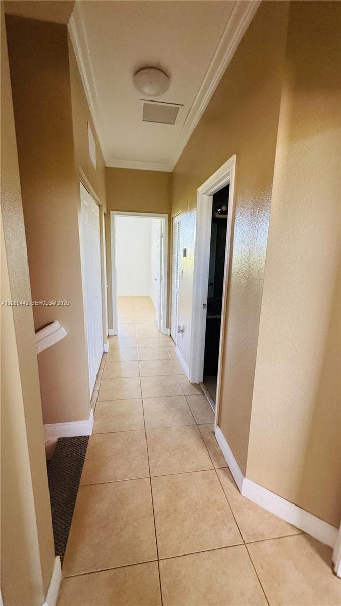 Hallway featuring neutral-toned walls, tile flooring, crown molding, and a flush-mount ceiling light fixture