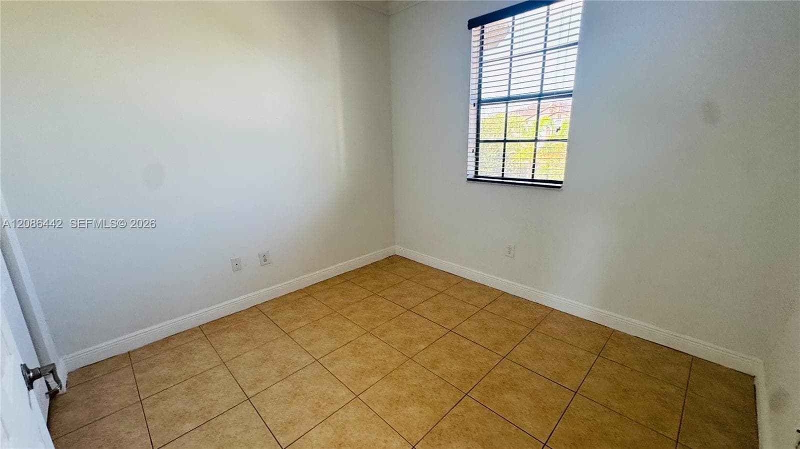 Interior room featuring neutral-toned walls, tile flooring, and a window equipped with horizontal blinds
