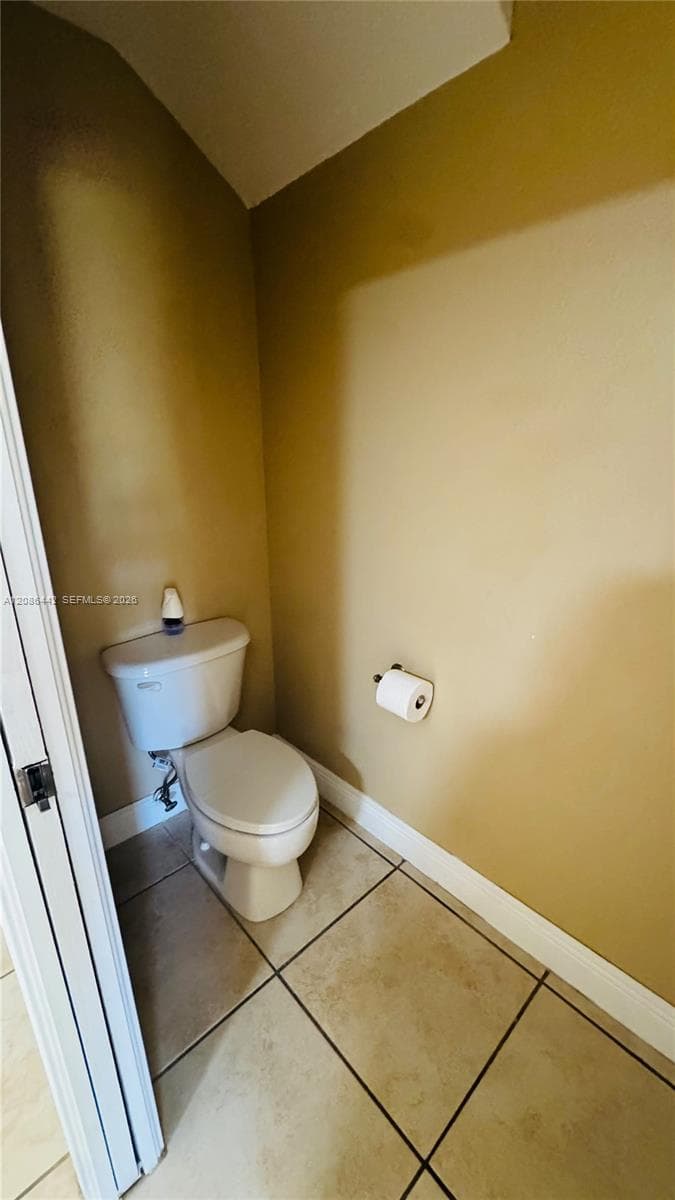 White porcelain toilet, large-format ceramic floor tile, and wall-mounted toilet paper dispenser