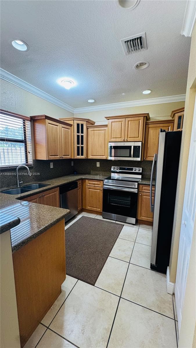 Kitchen featuring shaker-style wood cabinetry, stone-finish countertops, stainless steel appliances, dual-basin sink, and ceramic tile flooring