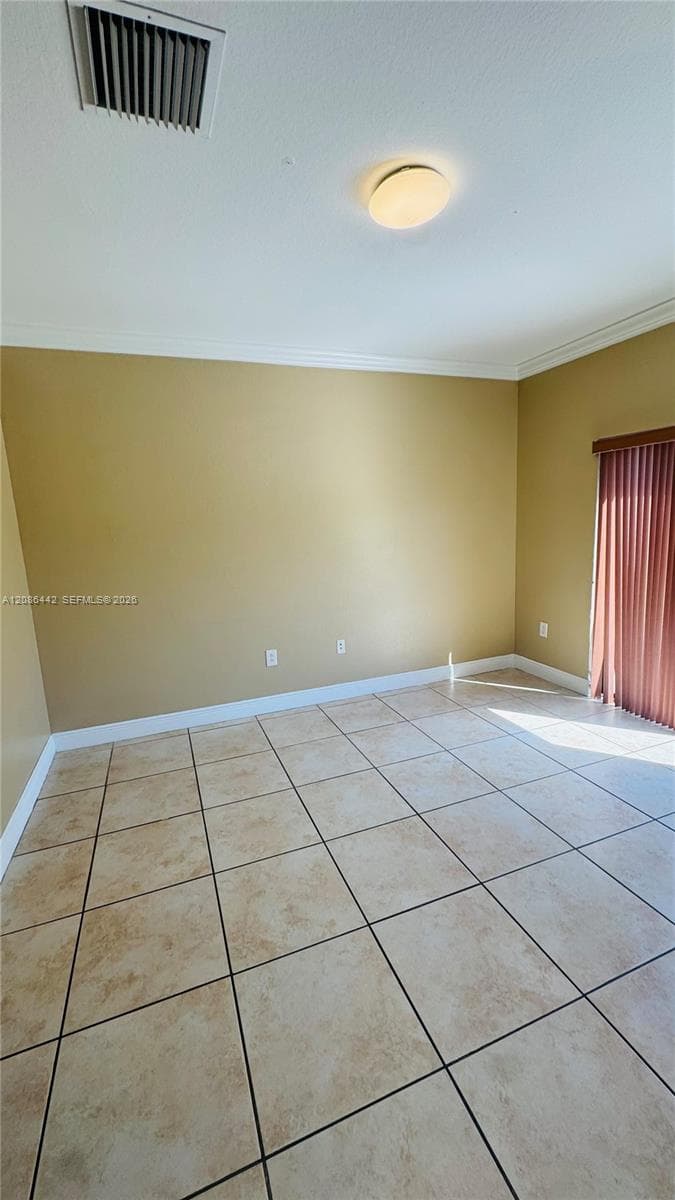 Neutral-toned interior room featuring large-format tile flooring, crown molding, a flush-mount light fixture, and vertical blinds