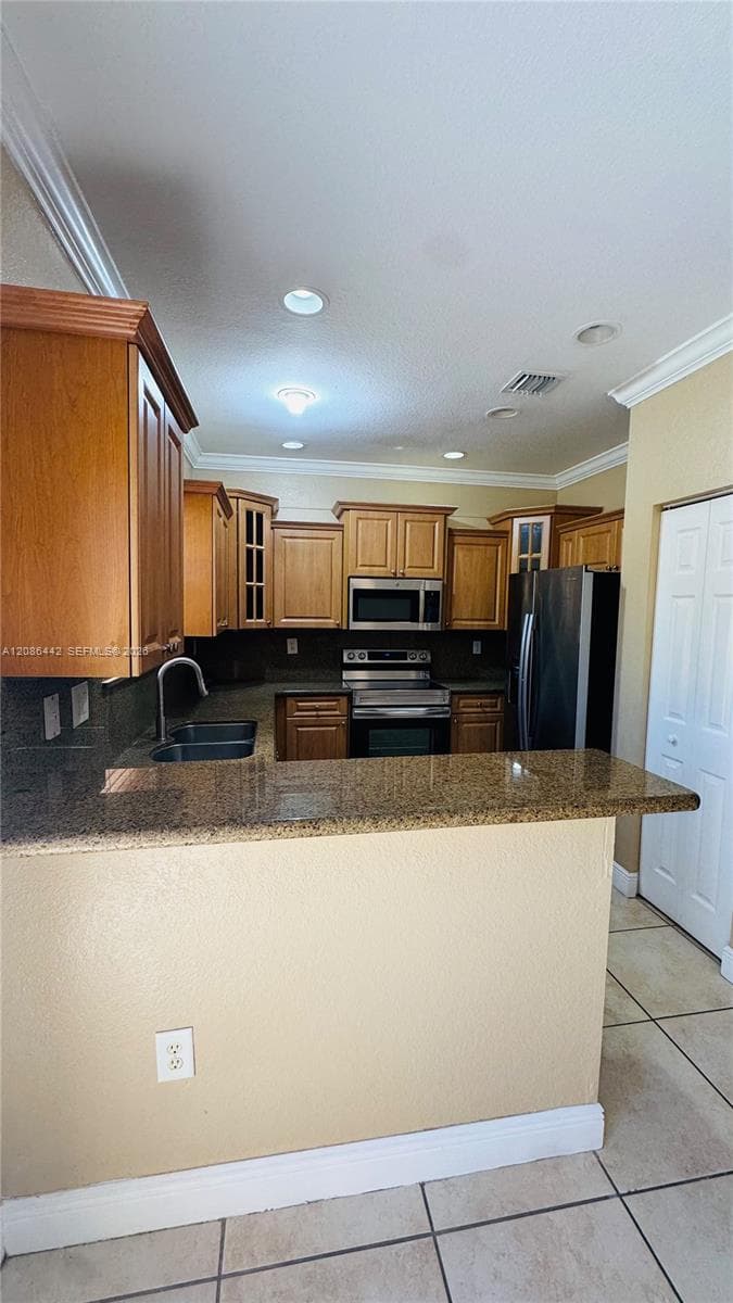 Kitchen featuring a peninsula with stone-finish countertops, stainless steel appliances, recessed ceiling lighting, crown molding, and tiled flooring