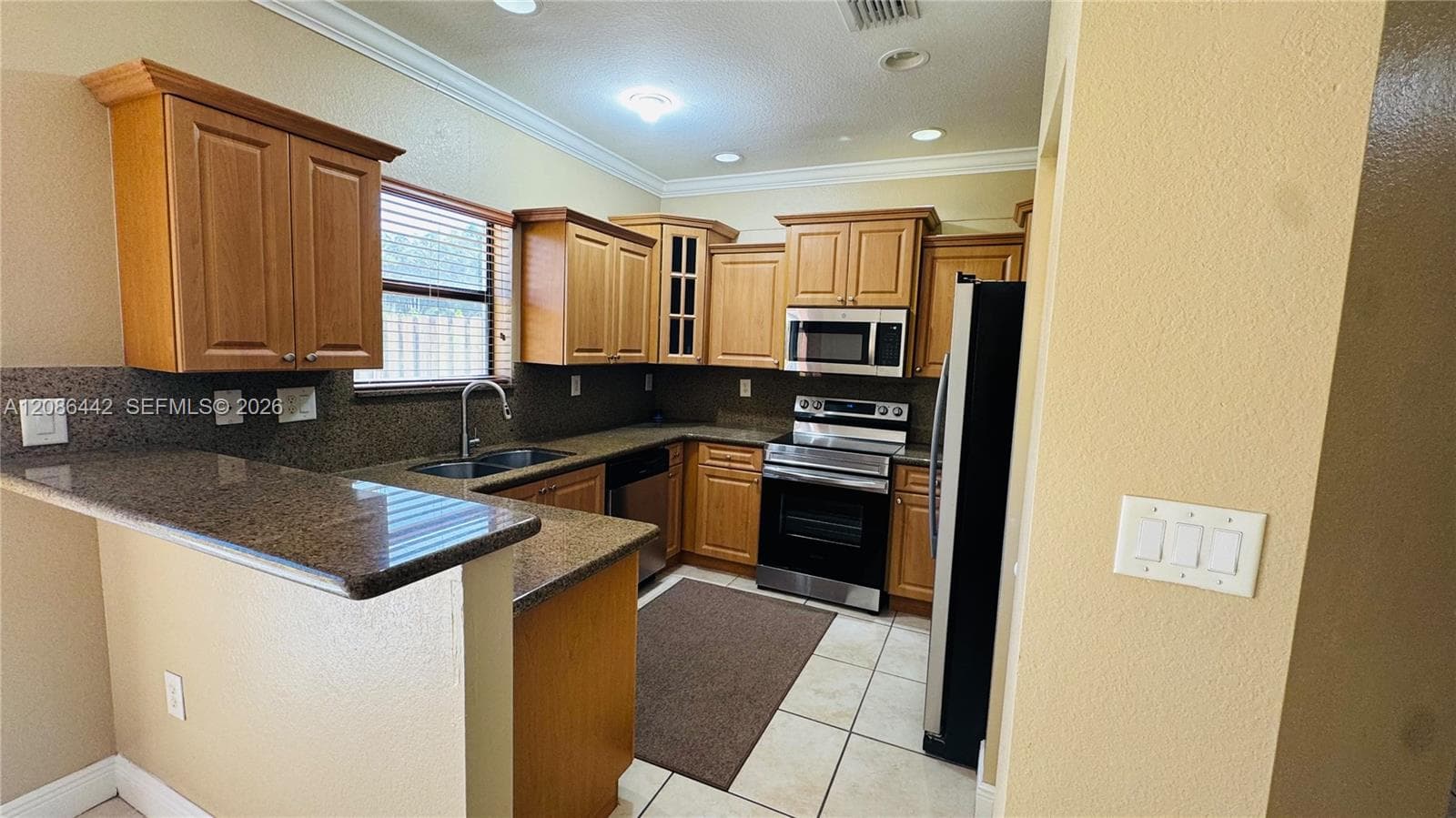 Kitchen featuring wood cabinetry, stone-surface countertops, stainless steel appliances, a double-basin sink, and tile flooring
