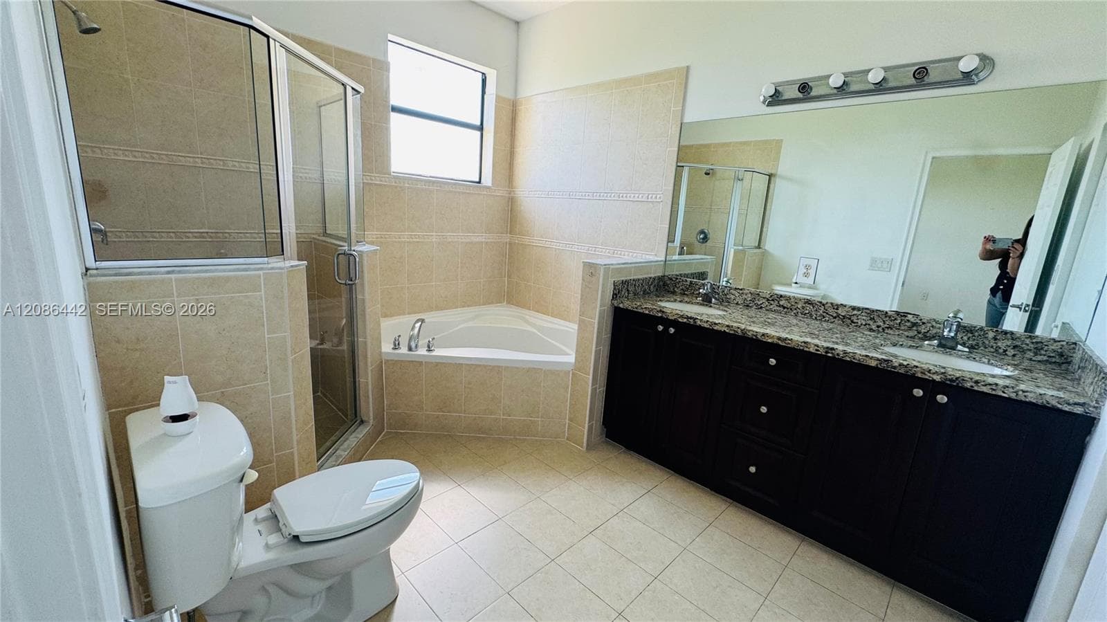 Bathroom featuring a dual-sink vanity with dark cabinetry, stone-surface countertops, a corner soaking tub, and a glass-enclosed shower