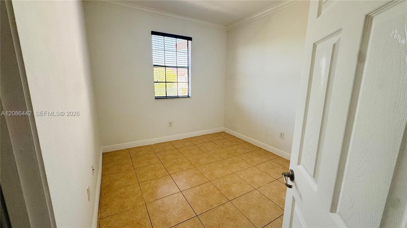 Neutral interior space featuring ceramic tile flooring, a single-pane window, crown molding, and a six-panel interior door