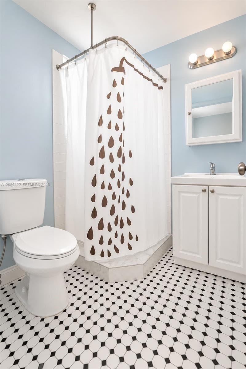 Bathroom featuring a vanity with integrated sink, recessed medicine cabinet, three-light vanity fixture, corner shower enclosure, and geometric patterned tile flooring