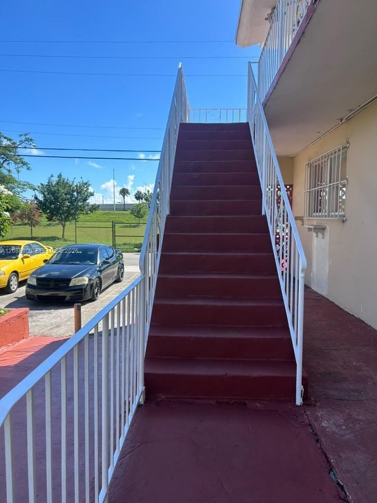 Exterior staircase featuring painted concrete steps, white metal handrails, and matching white metal security bars on the window