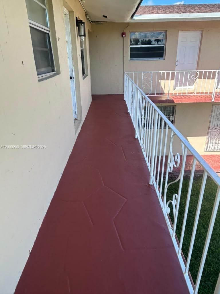 Exterior walkway featuring a painted concrete floor, decorative metal railings, wall-mounted lighting, and multi-pane windows