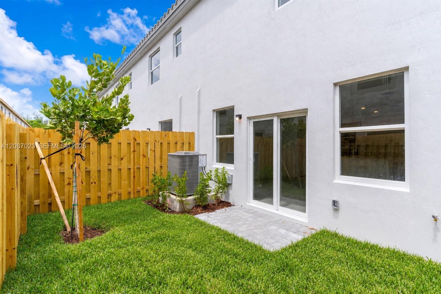 Stucco exterior featuring a wood-panel fence, paver patio, sliding glass door, and green space