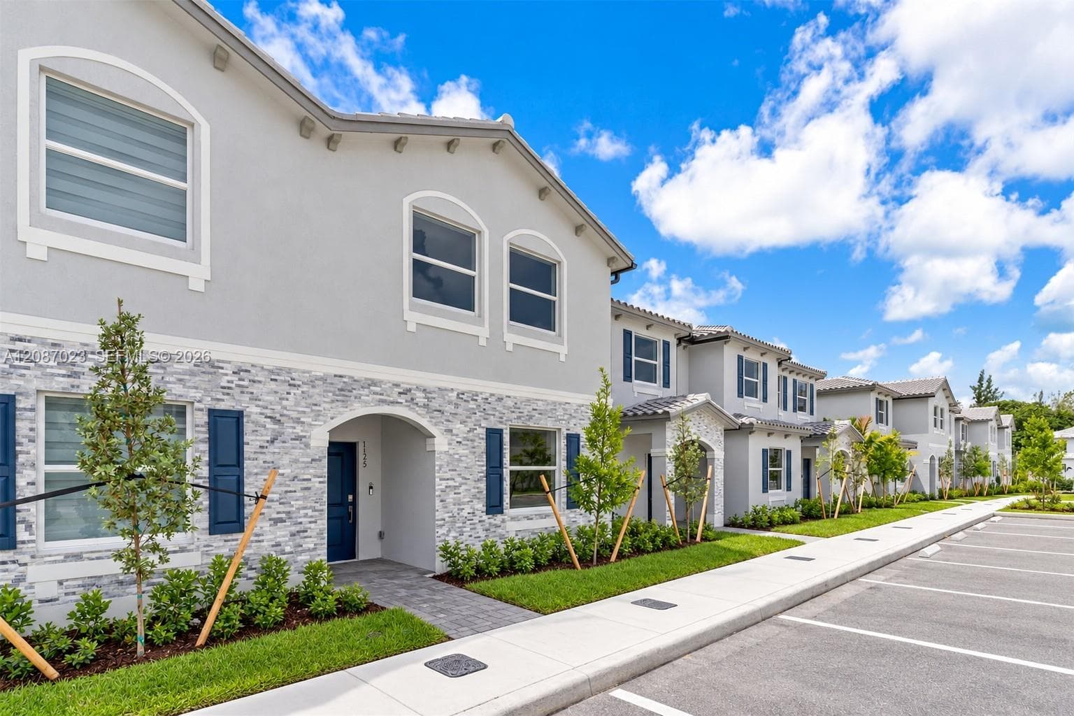 Exterior facade featuring light-toned stucco, multi-textured stone veneer, arched window detailing, dark blue shutters, and paved walkways