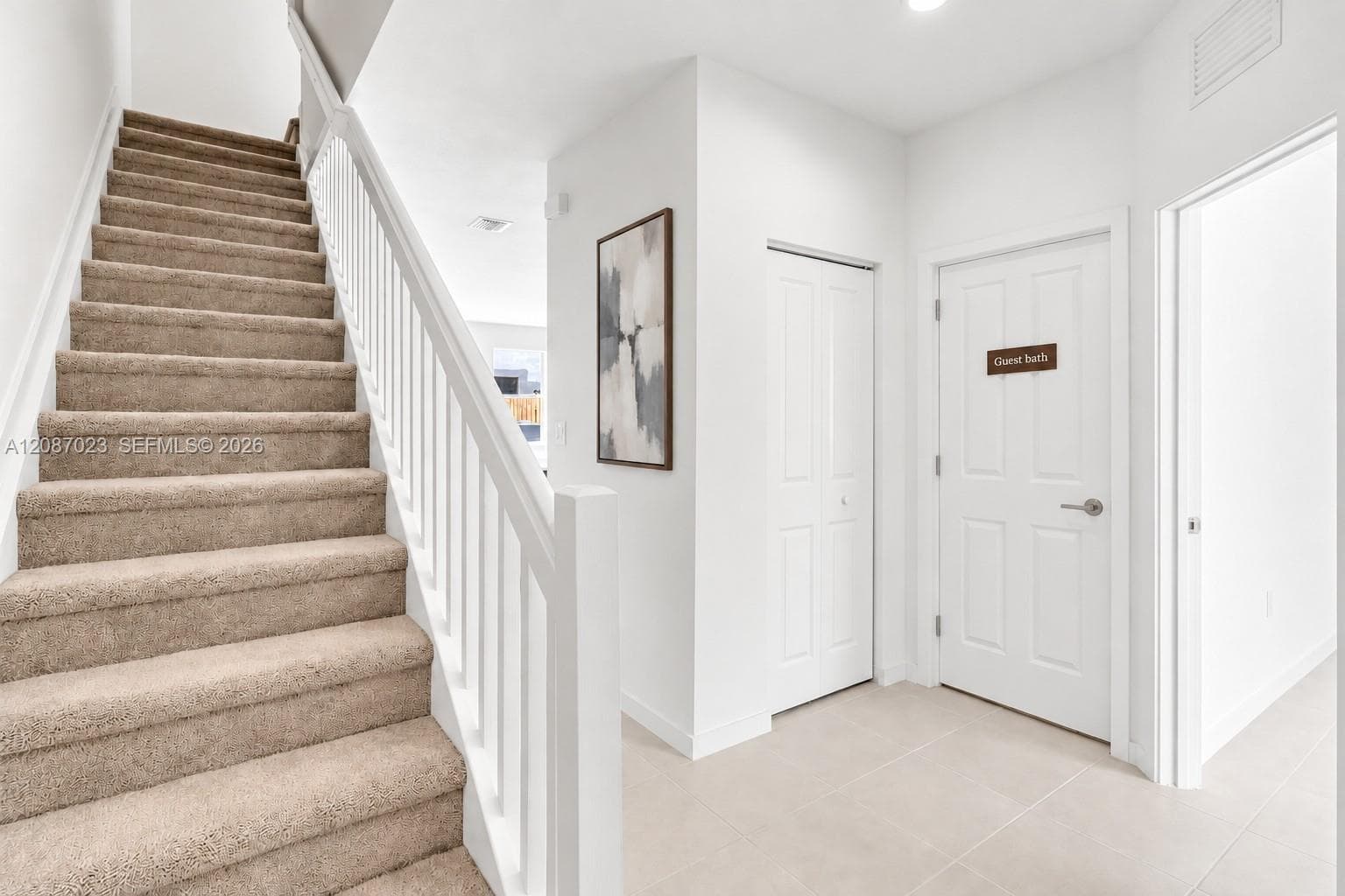 Foyer featuring neutral tile flooring, a carpeted staircase with a white handrail, and white panel doors