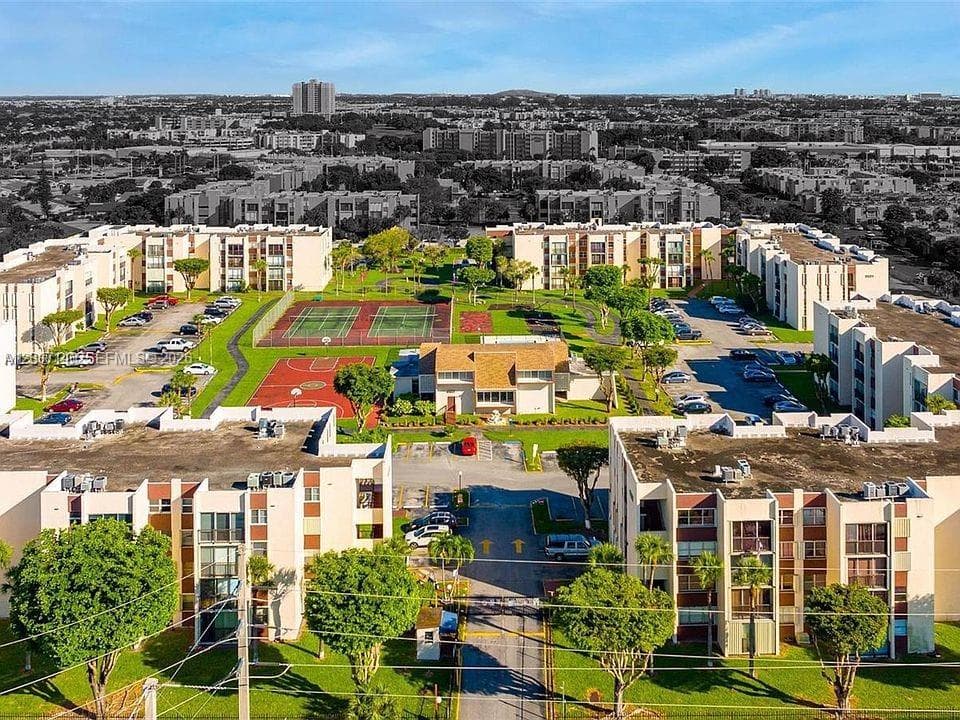 Aerial perspective of the complex featuring tennis courts, a basketball court, sprawling landscaped lawns, mature trees, and designated surface parking