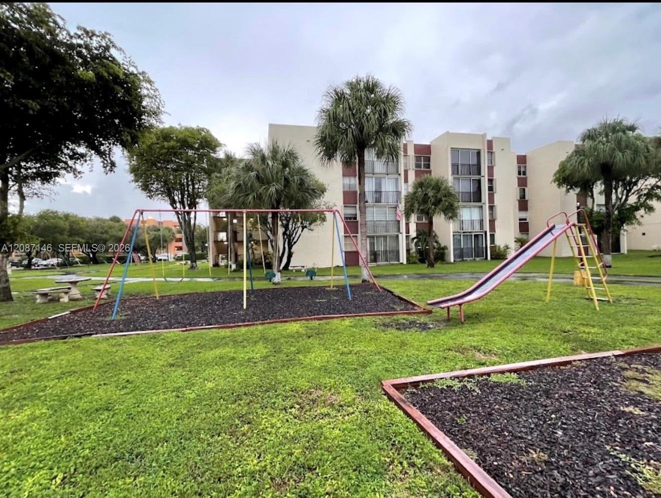 Outdoor recreational space featuring a swing set, metal slide, and manicured green lawn with mature palms