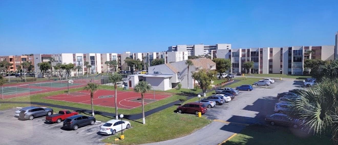 Exterior grounds featuring a paved basketball court, fenced tennis court, asphalt parking area, and mature palm trees