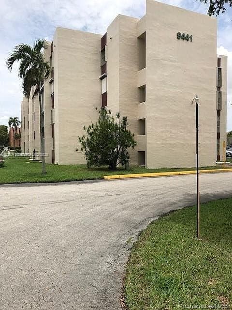 Multi-story residential building featuring a stucco exterior, vertical architectural recessed columns, and mature palm tree landscaping