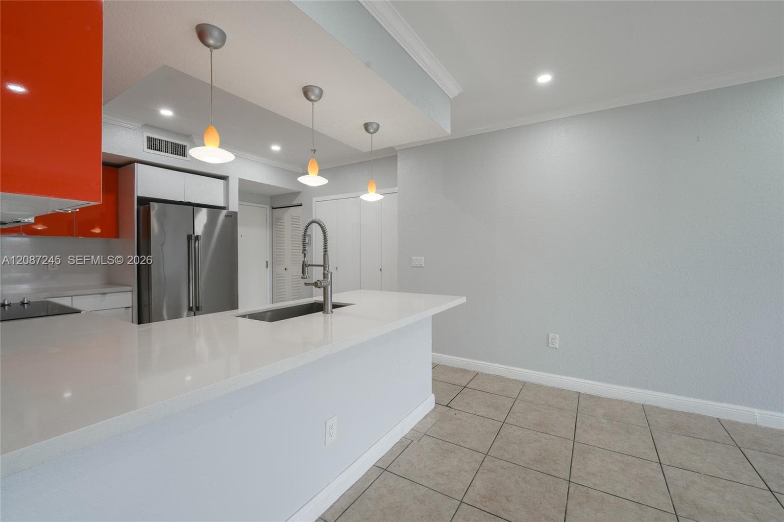 Kitchen featuring a quartz countertop island with an integrated sink and gooseneck faucet, high-gloss orange cabinetry, stainless steel refrigerator, and three pendant light fixtures over the workspace