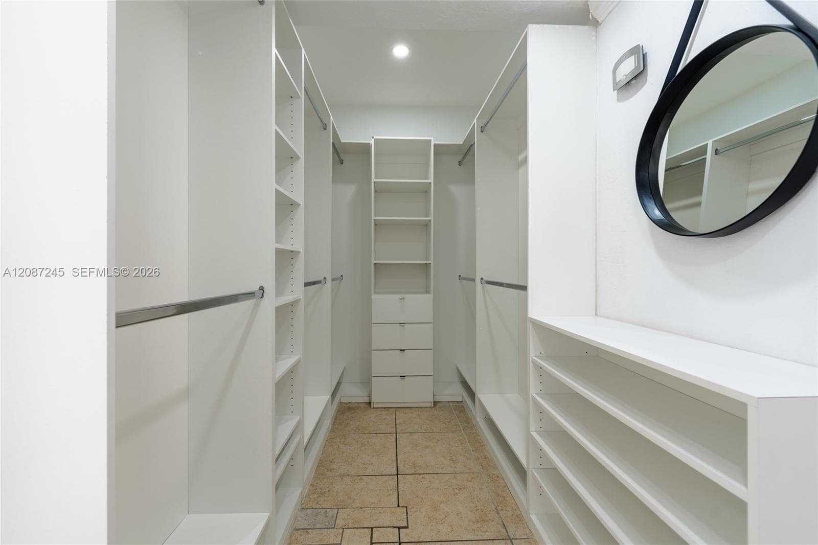 Custom reach-in closet system featuring white floor-to-ceiling shelving, built-in dresser drawers, hanging rods, and open shoe storage, accented by tile flooring and recessed lighting