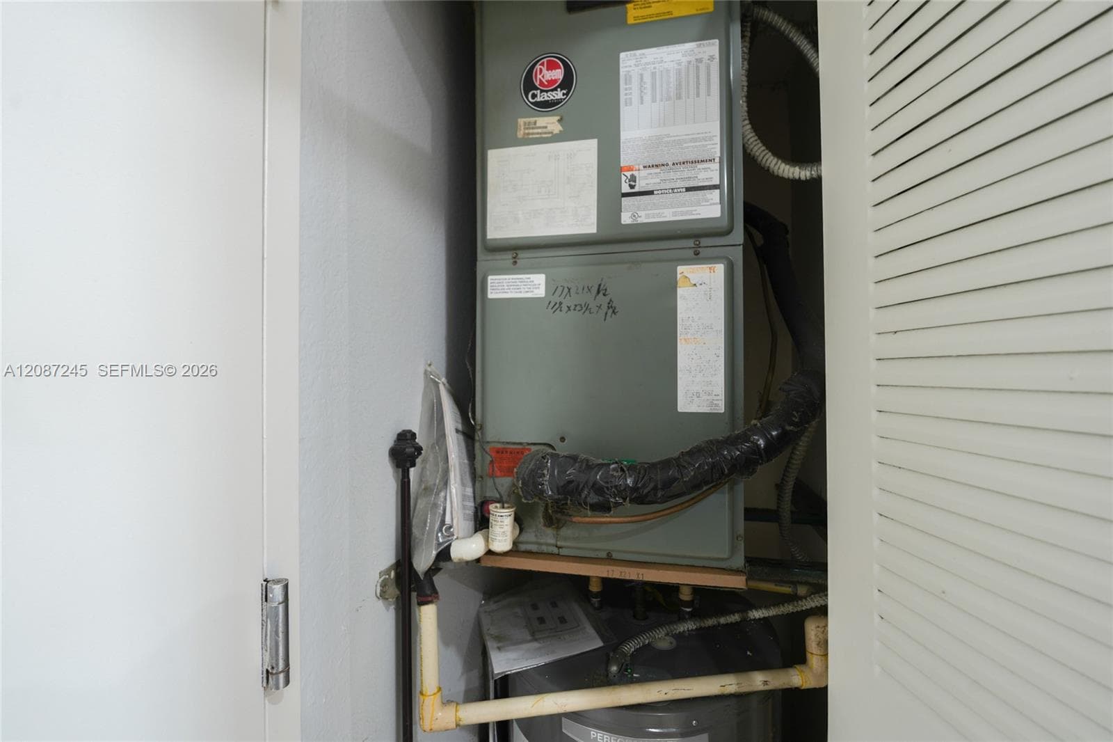 Mechanical closet featuring a Rheem Classic HVAC air handler and a water heater enclosed by a louvered door