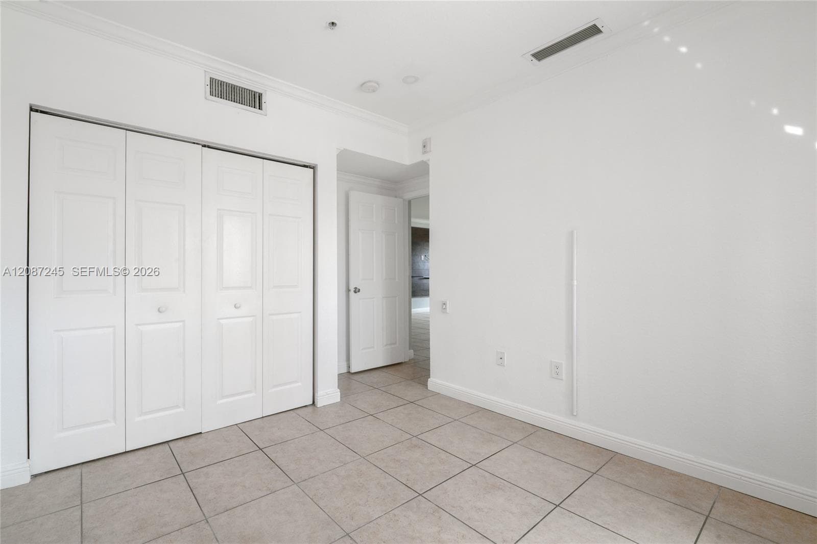 Interior space featuring large-format tile flooring, multi-panel bi-fold closet doors, and crown molding