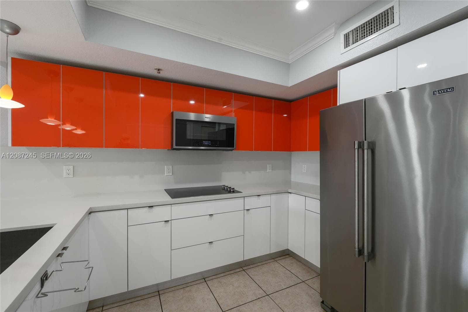 Modern kitchen featuring high-gloss orange upper cabinetry, white lower cabinetry, solid-surface countertops, stainless steel appliances, and tile flooring