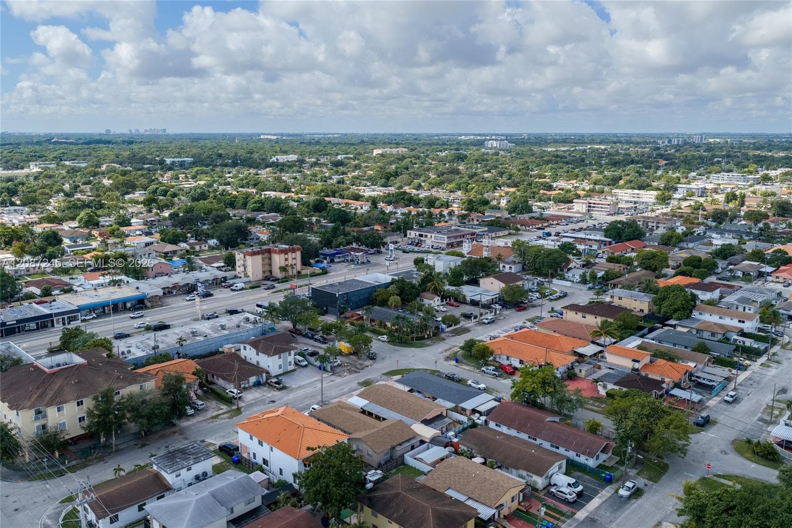 Aerial perspective featuring an established urban environment with a mix of residential and commercial structures, paved roadways, and dense tree canopy