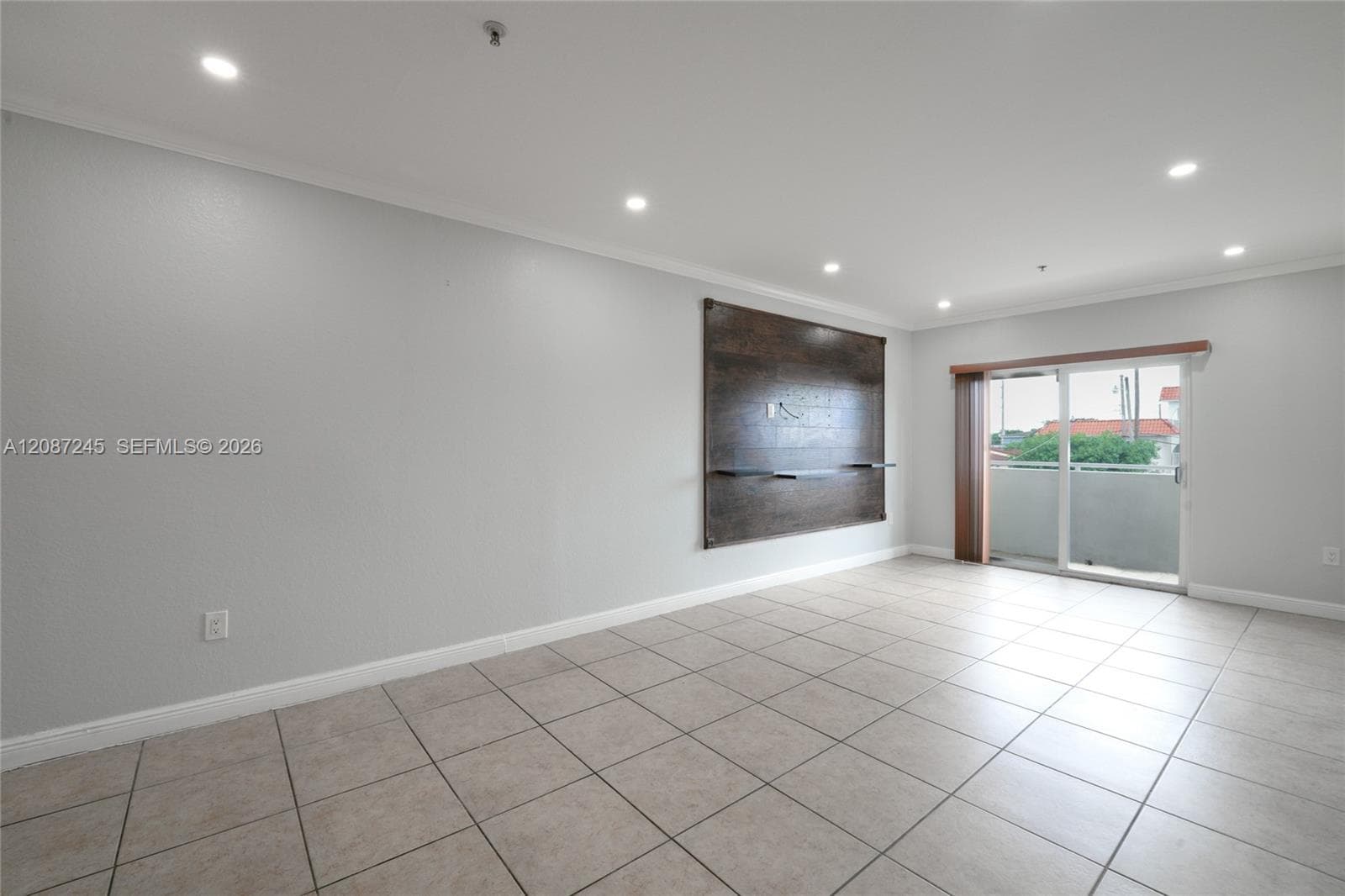 Open-concept living space featuring large-format ceramic tile flooring, recessed ceiling lighting, and a built-in wood-finish media accent wall with integrated shelving