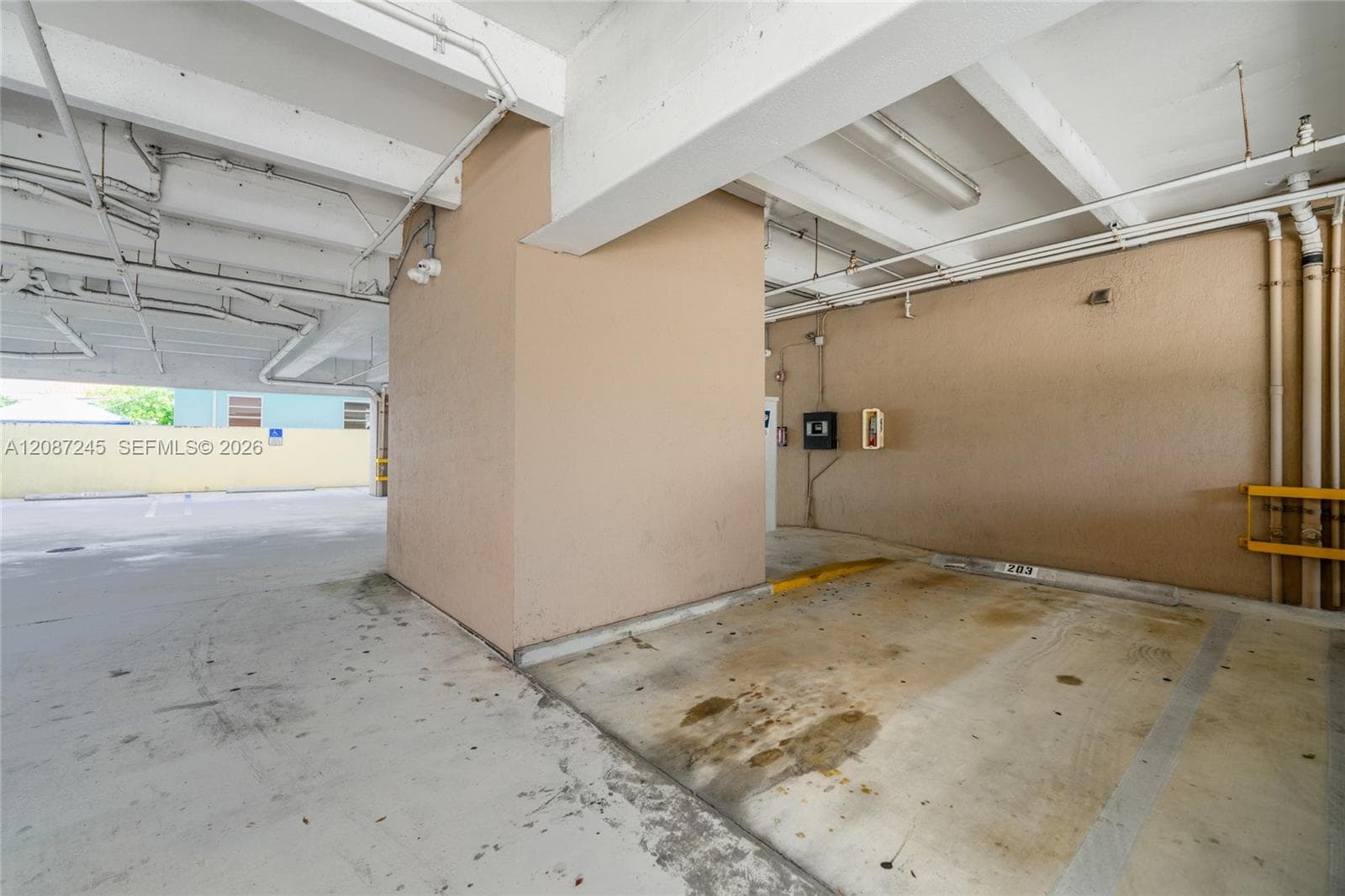 Covered parking space featuring a concrete floor, exposed structural ceiling beams, and wall-mounted electrical hardware