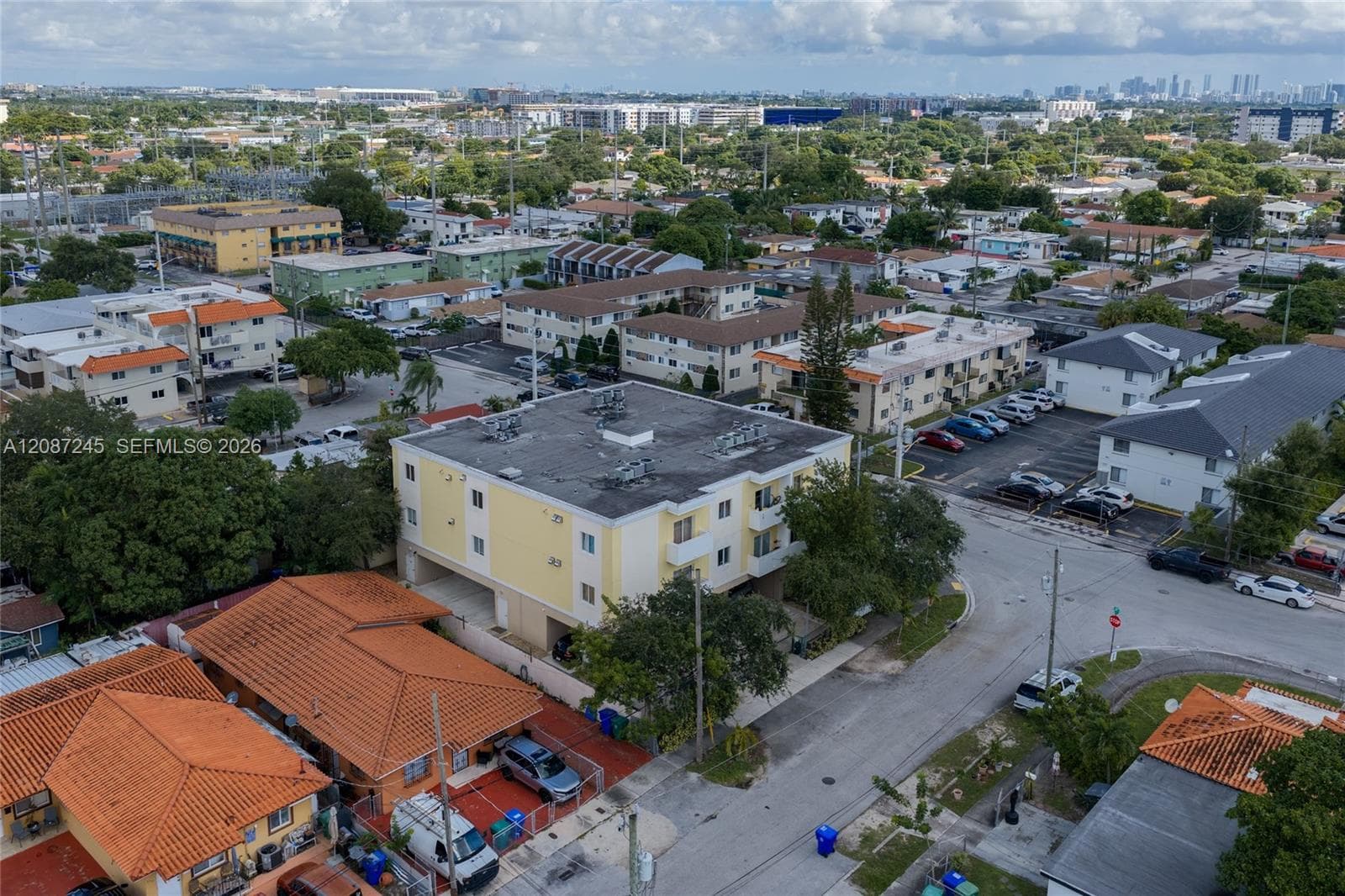Three-story residential building featuring a yellow stucco exterior, flat roof, and ground-level covered parking area situated in an urban setting