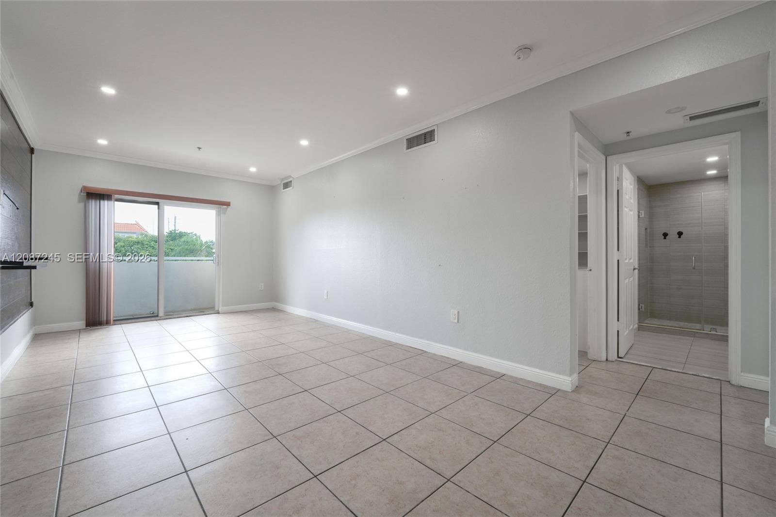 Neutral interior space featuring large-format tile flooring, recessed ceiling lighting, and sliding glass door access to an exterior balcony