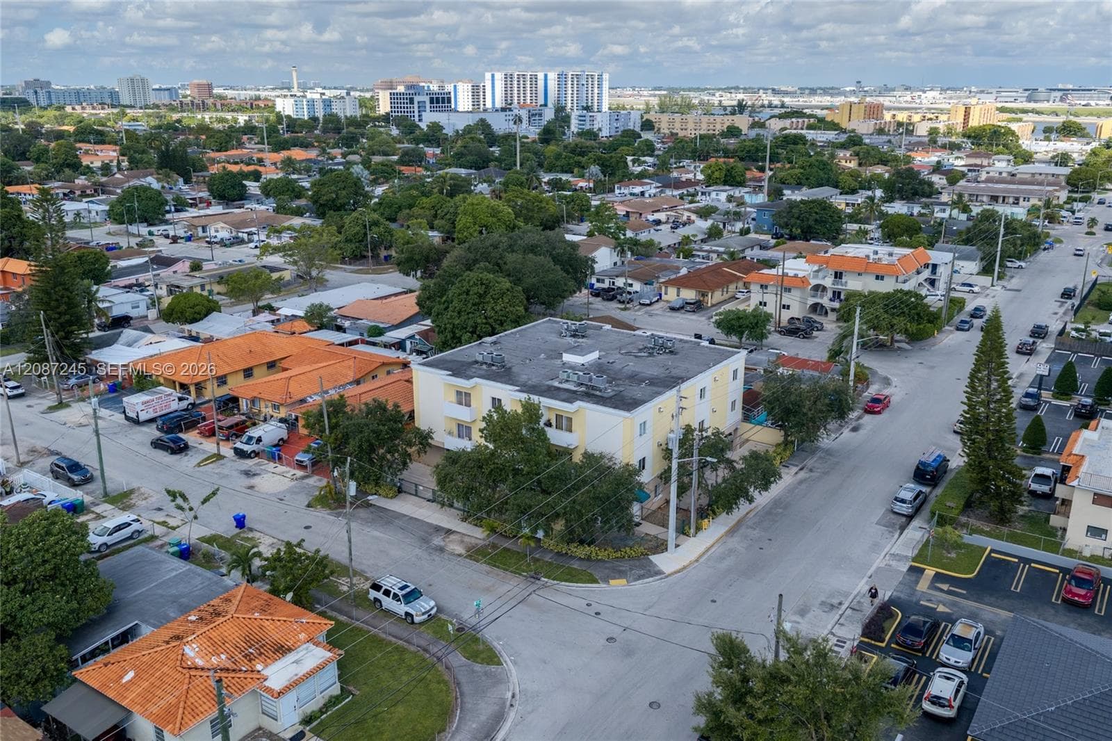 Multi-story residential building featuring a flat roof and light-colored stucco exterior, situated on a corner lot with mature landscaping