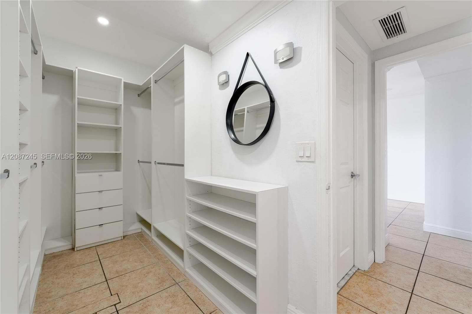 Walk-in closet featuring white custom built-in cabinetry, integrated shelving units, multi-tier drawer stacks, and tile flooring