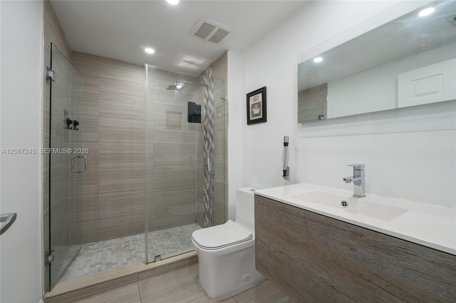 Modern floating vanity with a seamless integrated sink, walk-in glass shower enclosure, decorative mosaic tile accent wall, stone-patterned floor tile, and recessed lighting