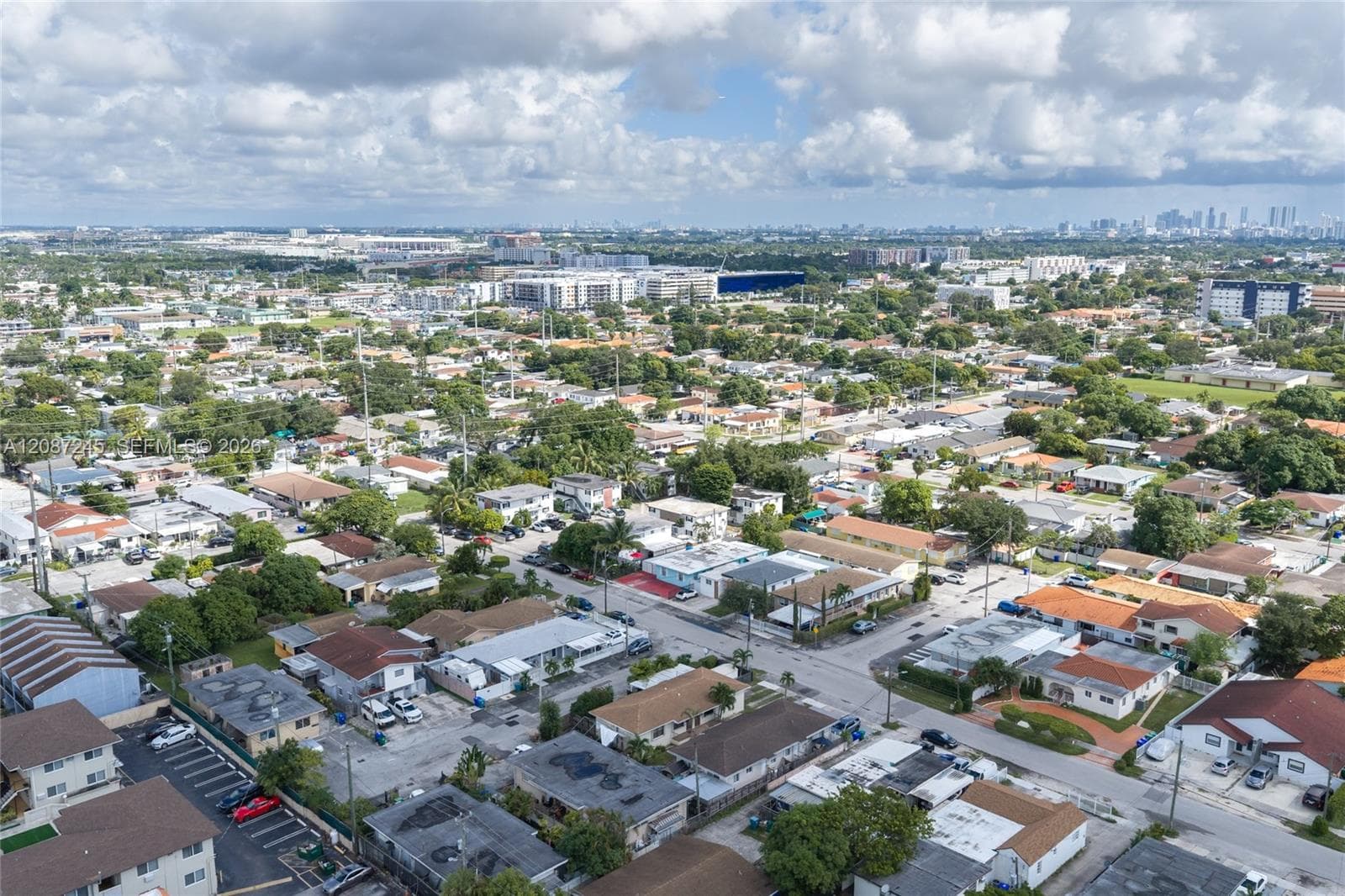 Aerial perspective showcasing urban surroundings, paved street infrastructure, low-rise residential development, and dense mature tree canopy